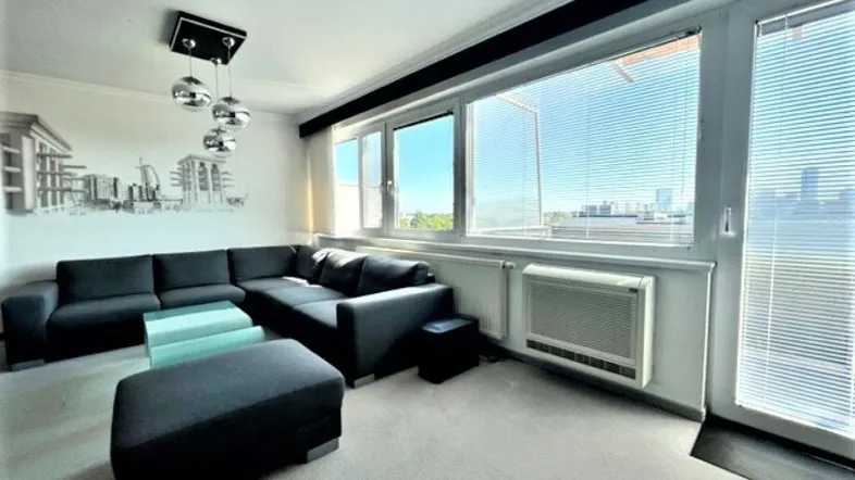 Helles Wohnzimmer mit großem Ecksofa, Teppichboden und weitem Blick durch die Fenster.