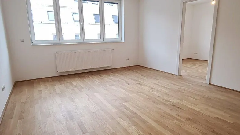Helles Zimmer mit Parkettboden, weißen Wänden und großem Fenster, bereit zur individuellen Gestaltung.