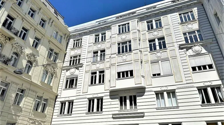 Die Fassade des Gebäudes zeigt klassische Architektur mit vielen Fenstern und einigen Rollläden.
