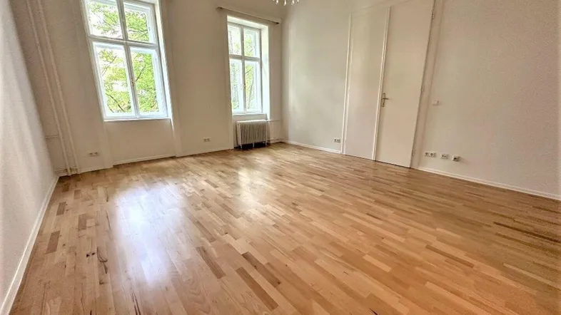 Geräumiges Zimmer mit hellem Parkettboden, hohen Fenstern und Kronleuchter.