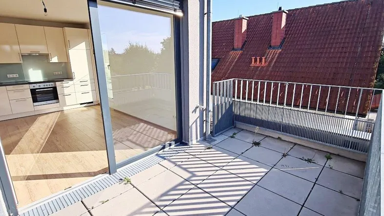 Geräumiger Balkon mit Fliesenboden und Blick auf die umliegenden Dächer und die Küche.