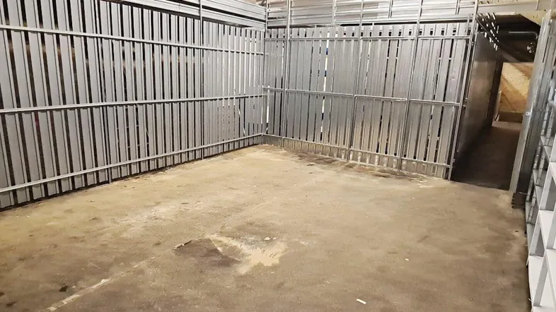 Geräumiger Kellerraum mit Metallabtrennungen, Betonboden und sichtbaren Ziegelwänden, ideal als Lagerfläche.