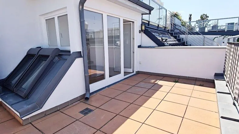 Geräumige Dachterrasse mit Fliesenboden und Zugang zu einem Raum mit Dachfenstern.