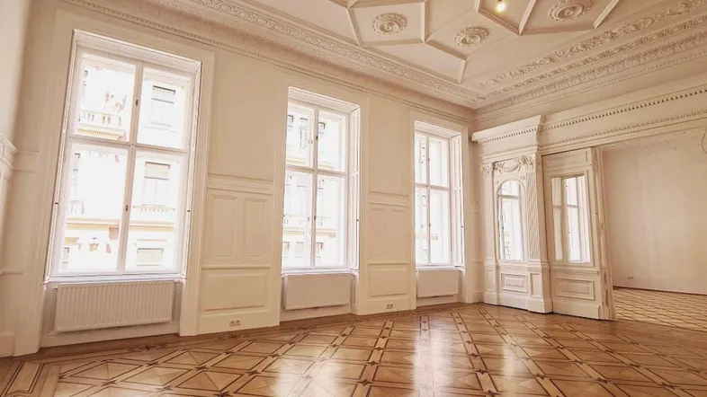 Großzügiges Wohnzimmer mit aufwendigem Parkettboden, hohen Decken und Stuckverzierungen.