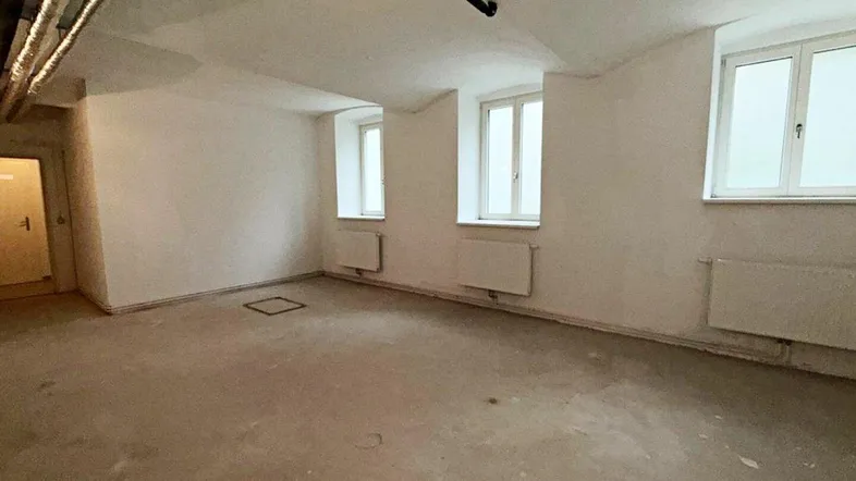 Geräumiger Kellerraum mit Betonboden, weißen Wänden, Heizkörpern und sichtbaren Leitungen an der Decke.