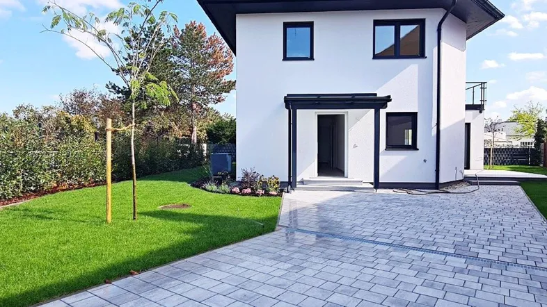 Modernes Einfamilienhaus mit weißer Fassade, gepflasterter Auffahrt und gepflegtem Vorgarten.