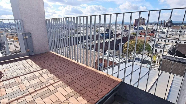 Geräumige Dachterrasse mit Holzdielen und weitem Blick über die Stadt und den Himmel.