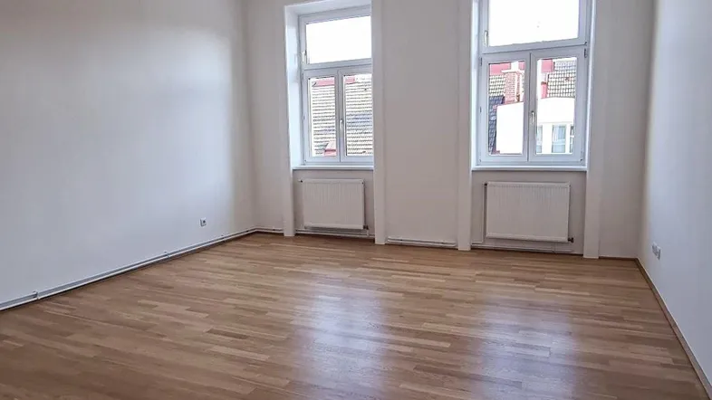Helles Zimmer mit Parkettboden und zwei Fenstern, ideal als Wohn- oder Schlafzimmer nutzbar.