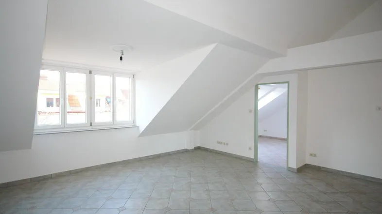 Heller Raum im Dachgeschoss mit Fliesenboden, schrägen Wänden und Fenster.