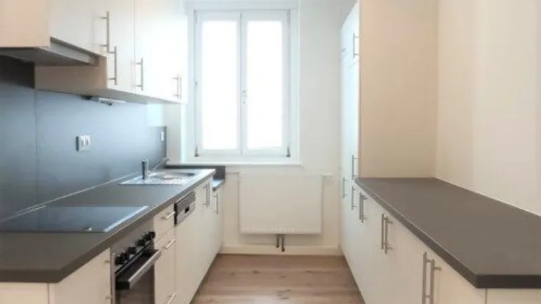 Moderne, helle Küche mit Holzparkettboden, weißen Schränken und dunkler Arbeitsplatte.
