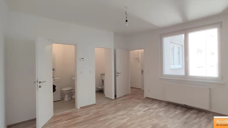 Heller Wohnraum mit Holzfußboden und großen Fenstern, der zu weiteren Zimmern führt.