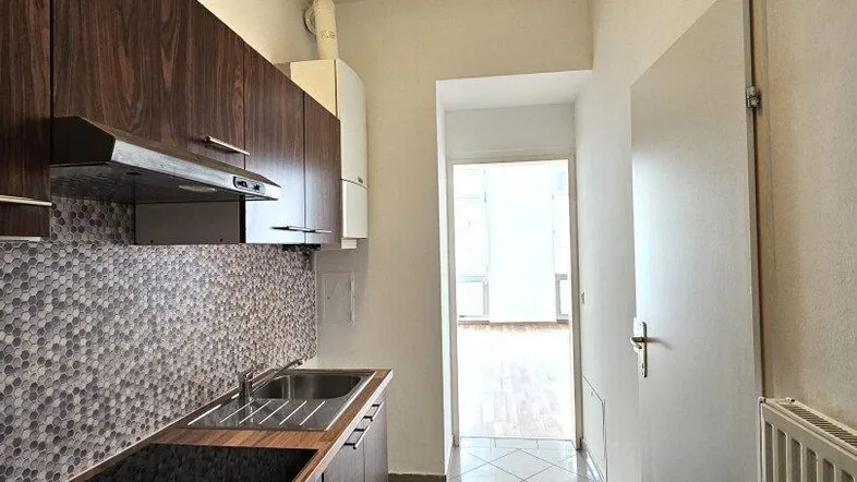 Schmale Küche mit dunklen Holzschränken, heller Arbeitsplatte, Induktionskochfeld und Fliesenboden.