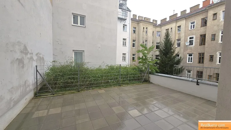 Große gepflasterte Terrasse im Innenhof mit Blick auf die umliegenden Gebäude und viel Grün.