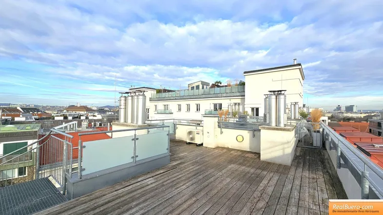 Weitläufige Dachterrasse mit Holzdielen und Blick auf die umliegenden Gebäude und den Himmel.