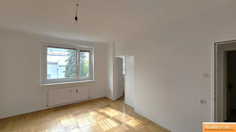 Helles Zimmer mit Fischgrätparkett, weißen Wänden und Fenster, bereit zur individuellen Gestaltung.