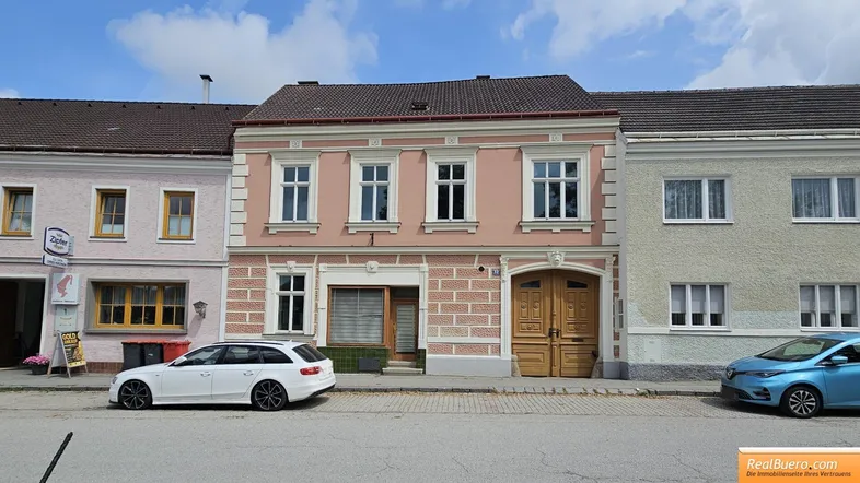 Rosa gestrichenes historisches Gebäude mit weißen Fensterrahmen und Holztüren an einer Straße.