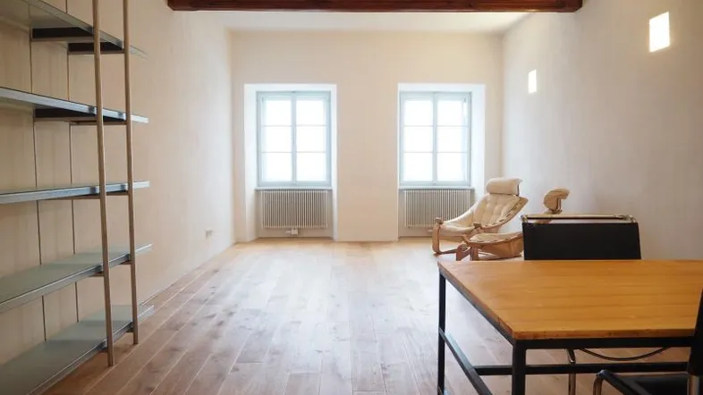 Helles, geräumiges Zimmer mit Holzbalken, Parkettboden und zwei Fenstern, ideal als Wohn- oder Arbeitsbereich.