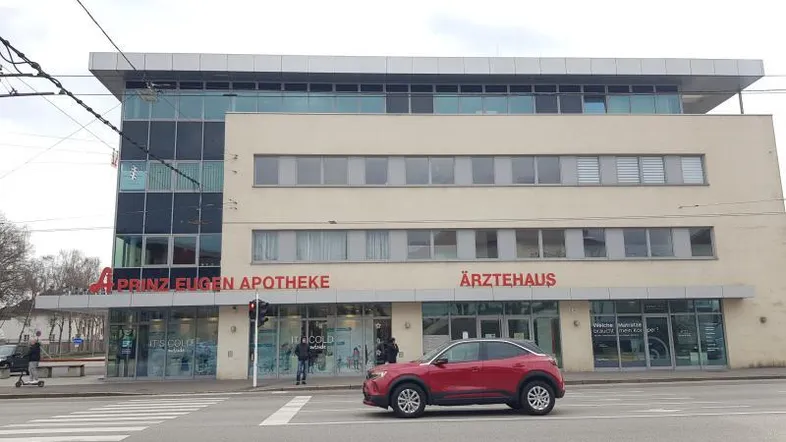 Modernes Geschäftsgebäude mit Apotheke und Ärztehaus im Erdgeschoss, an einer belebten Straße gelegen.