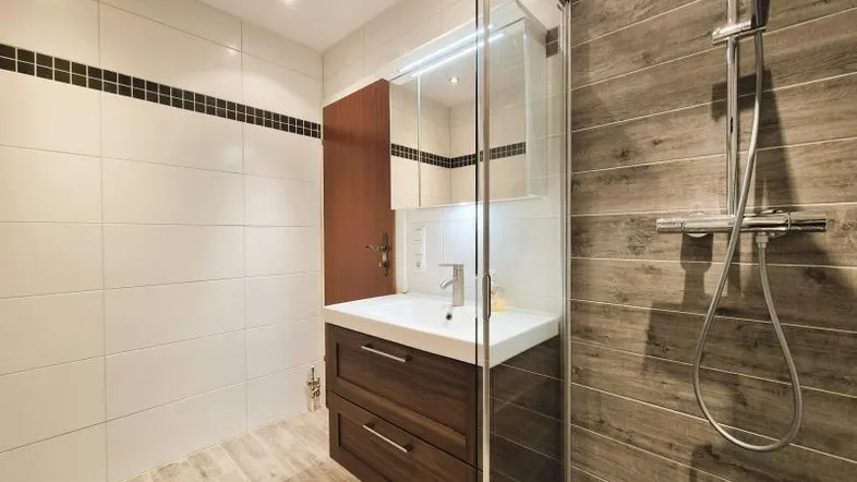 Modernes Badezimmer mit Holzwaschtisch, Spiegelschrank und ebenerdiger Dusche, hell gefliest.