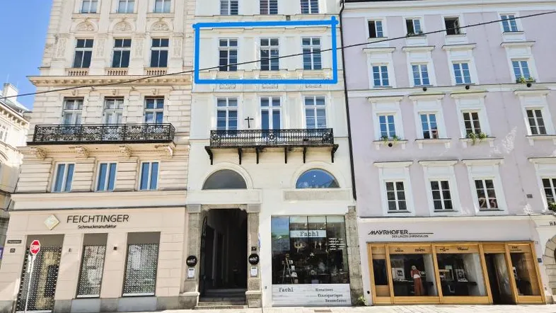 Historische Fassade eines Mehrfamilienhauses mit Geschäften im Erdgeschoss und Balkon im ersten Stock.
