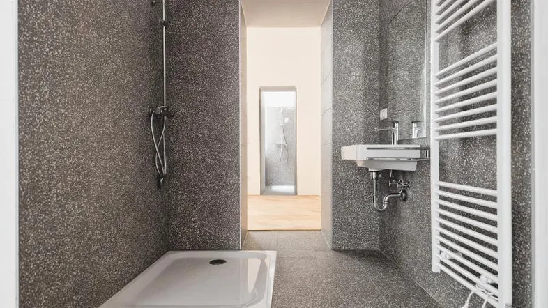 Modernes Badezimmer mit großformatigen grauen Fliesen, ebenerdiger Dusche und Handtuchheizkörper.