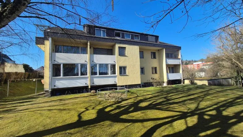 Mehrfamilienhaus mit gelber Fassade und großem Gartenbereich an einem sonnigen Tag.