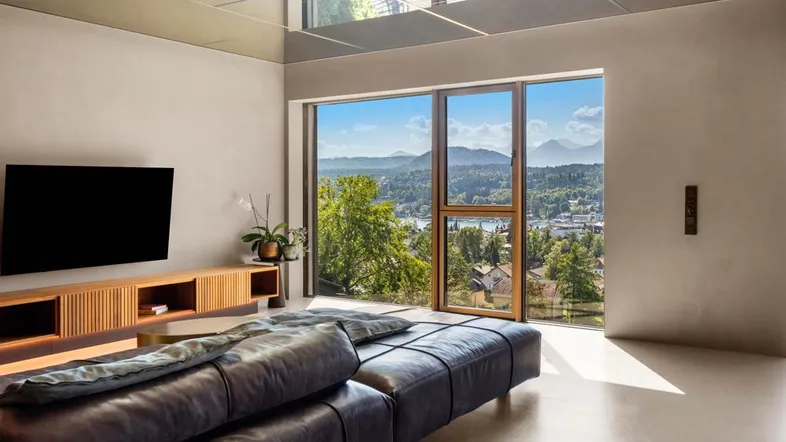 Helles, modernes Wohnzimmer mit großem Fenster, das einen weiten Blick auf See und Berge bietet.
