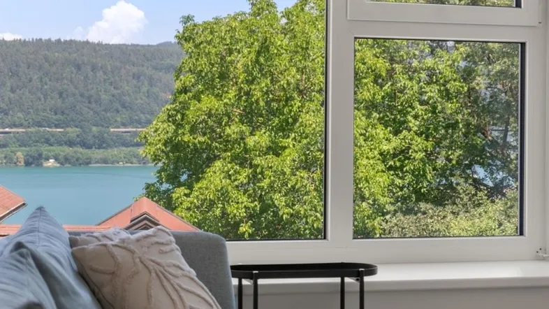Helles Wohnzimmer mit Seeblick durch große Fenster und grüner Umgebung.