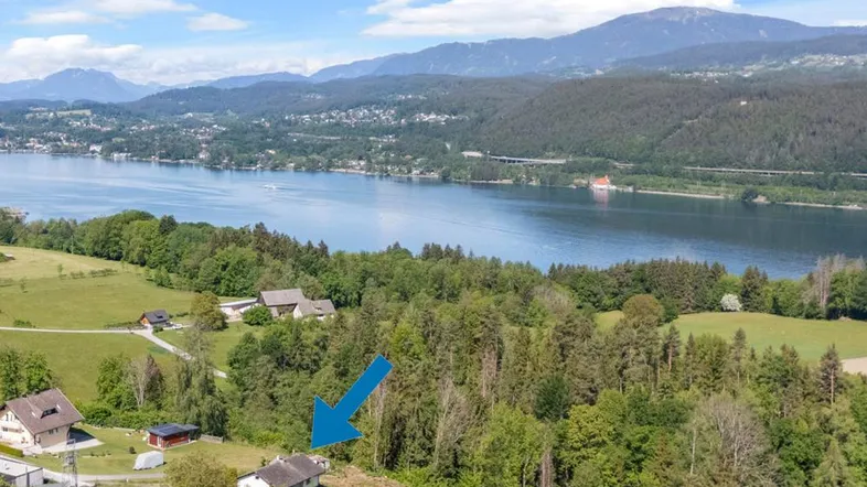 Luftaufnahme eines Hauses mit Seeblick und Bergpanorama, umgeben von viel Grün und Wald.