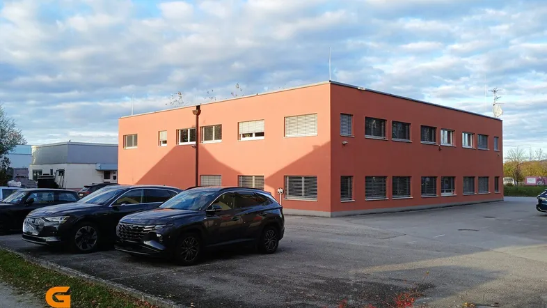 Modernes Bürogebäude mit oranger Fassade und ausreichend Parkplätzen unter einem bewölkten Himmel.