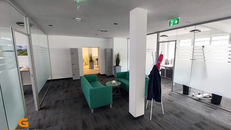 Gemütlicher Loungebereich im Büro mit grünen Sofas, Glastrennwänden und Teppichboden.