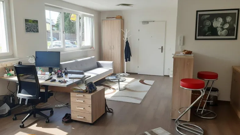 Heller Wohnbereich mit Arbeitsplatz, Sofa und kleiner Bar, ausgestattet mit Laminatboden und großen Fenstern.