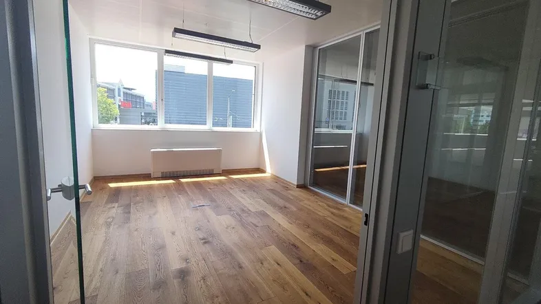 Heller Büroraum mit großen Fenstern, Holzboden und viel Tageslicht, ideal für eine moderne Arbeitsumgebung.