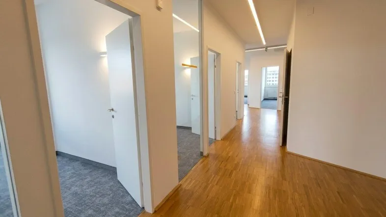 Langer Flur mit Holzboden und Zugang zu mehreren Büroräumen, beleuchtet durch moderne Deckenleuchten.