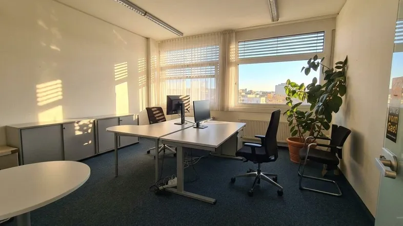 Helles Büro mit mehreren Arbeitsplätzen, Teppichboden und weitem Blick über die Stadt.