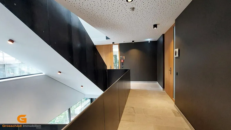 Modernes Treppenhaus mit dunklen Wänden, hellen Fliesen und großen Fenstern, die viel Tageslicht hereinlassen.