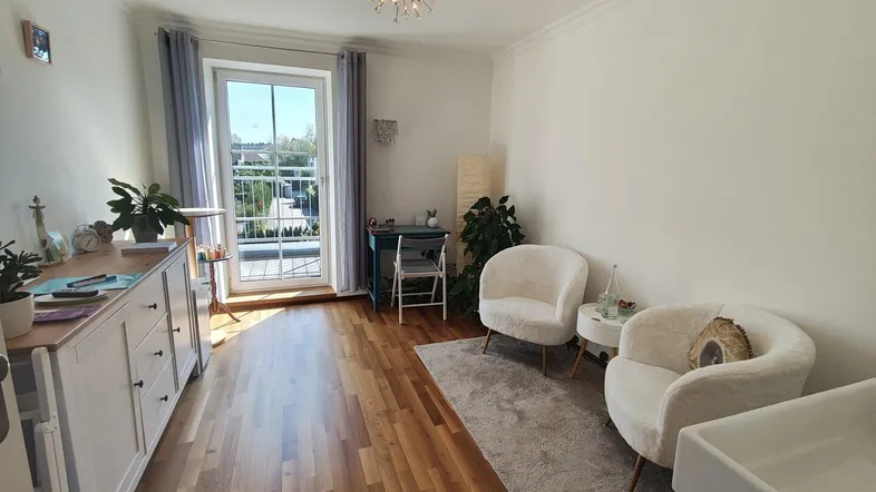 Helles Arbeitszimmer mit Holzboden, Balkonzugang und gemütlichen Sitzgelegenheiten, ideal für konzentriertes Arbeiten.