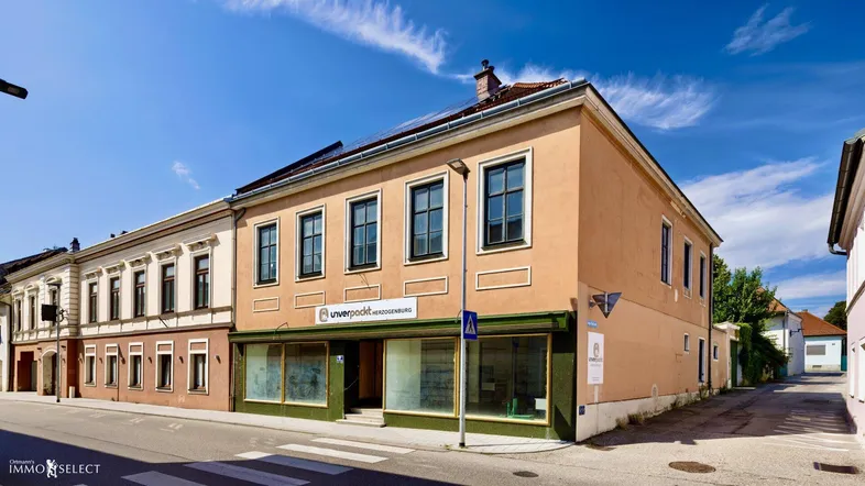 Fassade eines Gebäudes an einer Straße mit Geschäften im Erdgeschoss und blauem Himmel.