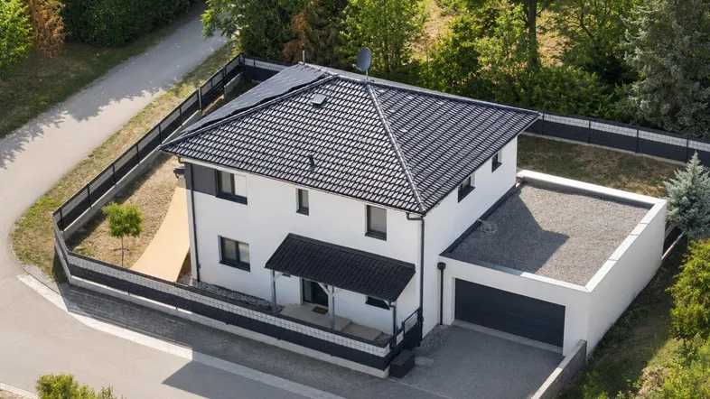 Luftaufnahme eines modernen Einfamilienhauses mit dunklem Dach, Solaranlage und Garage.