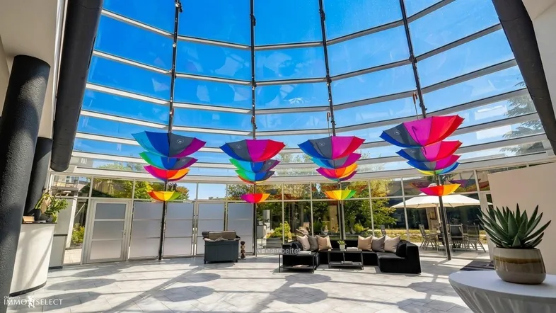 Großer, lichtdurchfluteter Wintergarten mit bunten Regenschirmen als Dekoration und bequemen Sitzgelegenheiten.