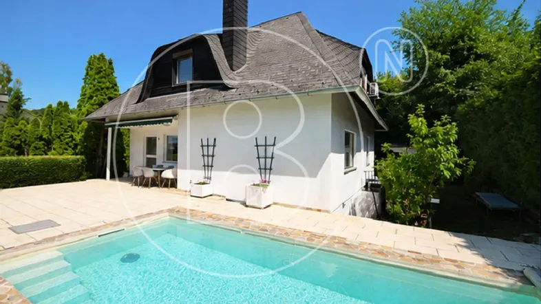 Außenansicht des Hauses mit Pool, gepflasterter Terrasse und Essbereich im Freien unter einer Markise.