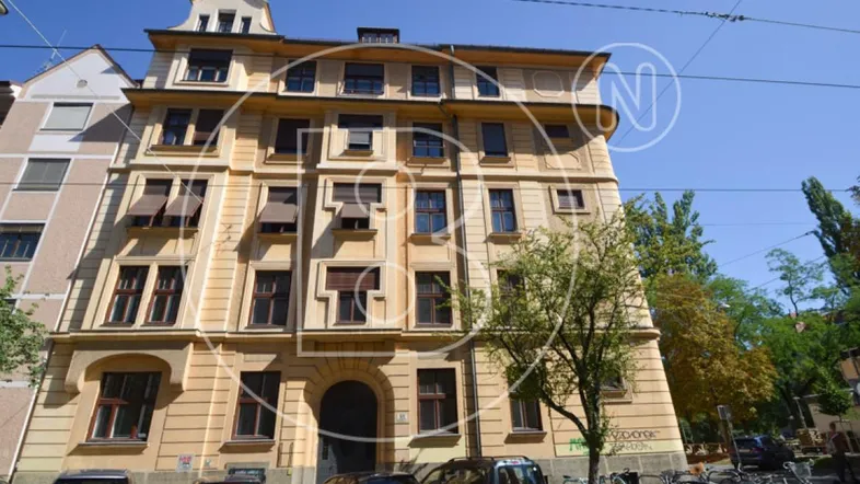 Fassade eines mehrstöckigen Wohngebäudes mit vielen Fenstern und Jalousien an einem sonnigen Tag.