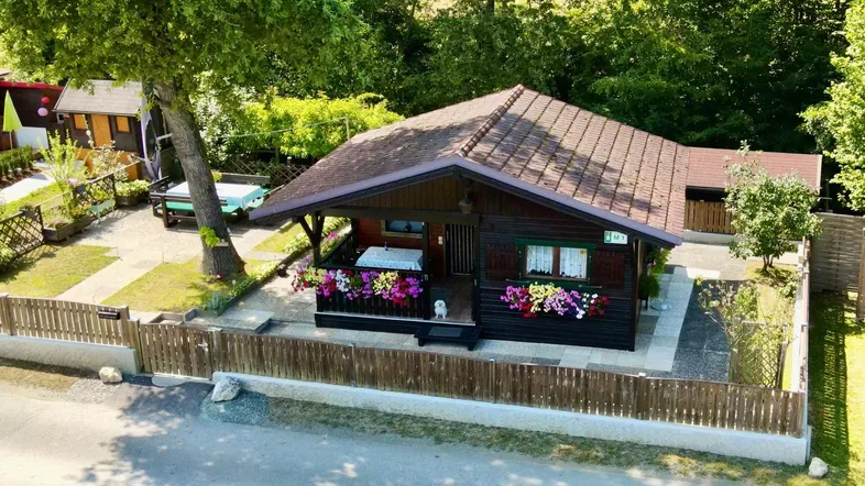 Gemütliches Holzhaus mit Blumenkästen und kleinem Vorgarten in ländlicher Umgebung.
