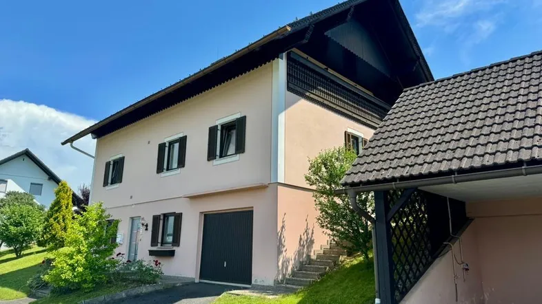 Ansicht des Hauses von vorne mit hellrosa Fassade, integrierter Garage und angrenzendem Carport.