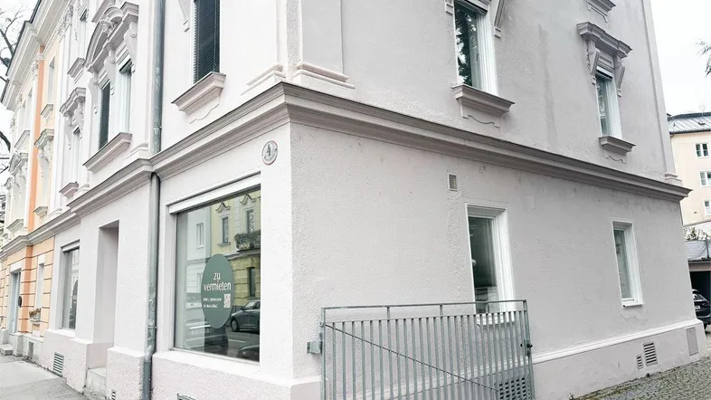 Eckansicht eines gepflegten Altbaus mit hellrosa Fassade und einem 'zu vermieten'-Schild im Schaufenster.
