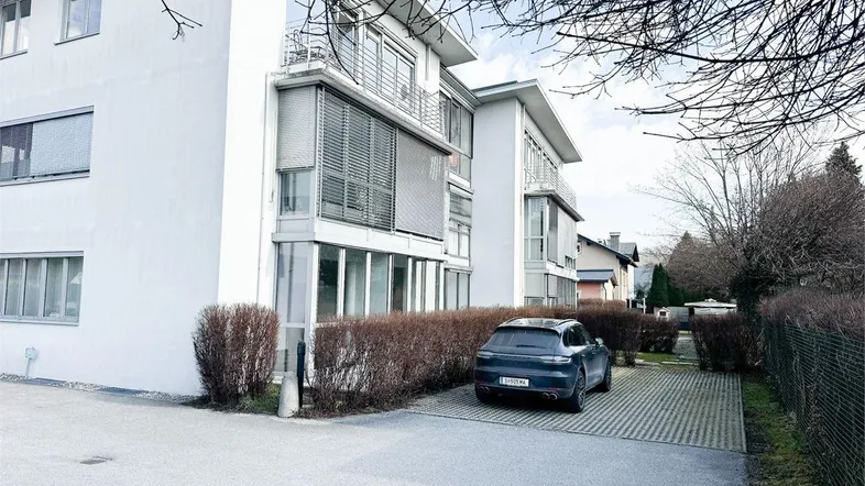 Modernes Mehrfamilienhaus mit großen Fenstern und Balkonen, umgeben von Hecken und Bäumen.