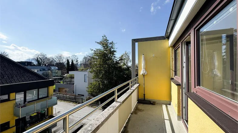 Heller Balkon mit Metallgeländer und Blick auf die umliegende Wohngegend unter blauem Himmel.