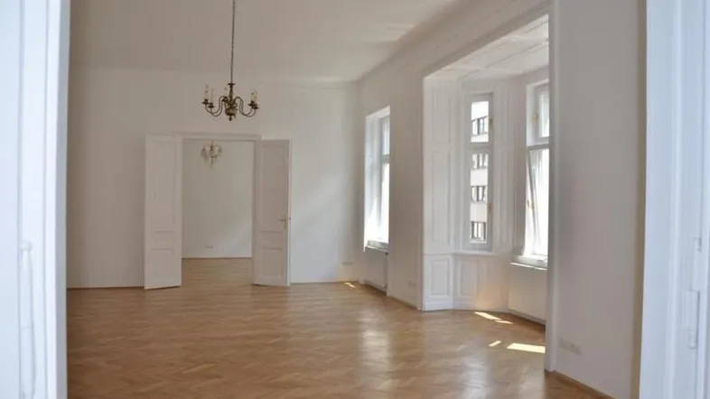 Helles Wohnzimmer mit Fischgrätparkett, hohen Decken und einem eleganten Kronleuchter.