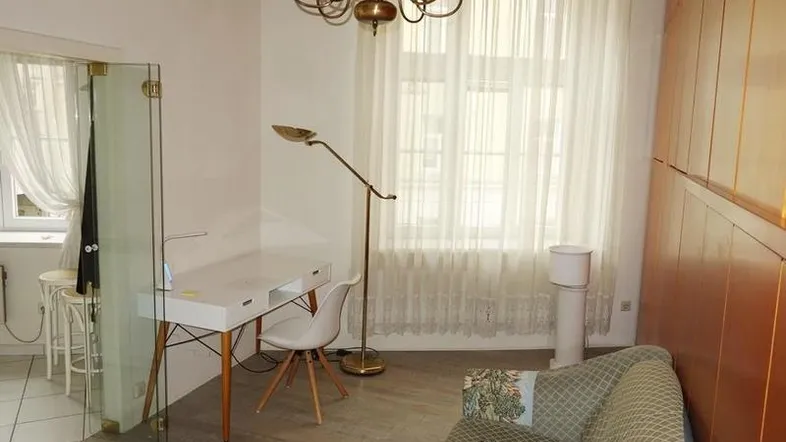 Helles Wohnzimmer mit Schreibtisch, Sofa, Holzvertäfelung und Kronleuchter.