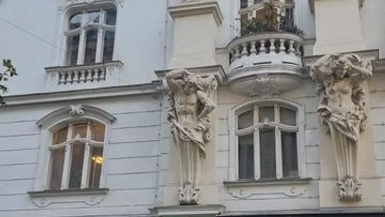 Klassisches Altbaugebäude mit reich verzierten Fassaden, Säulen und einem kleinen Balkon an einer belebten Straße.